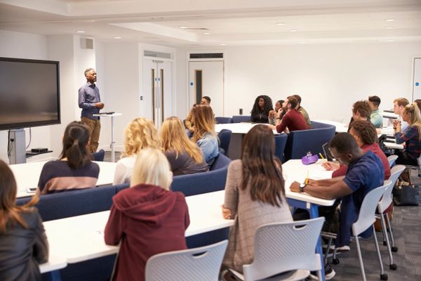 Instructor teaching diverse students in a modern classroom with a large screen.