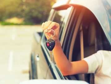 Person holding car keys out of a car window.