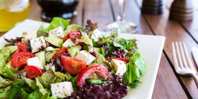 square plate with salad, tomatoes, avocado, on table with fork next to plate & vinegarette dressing