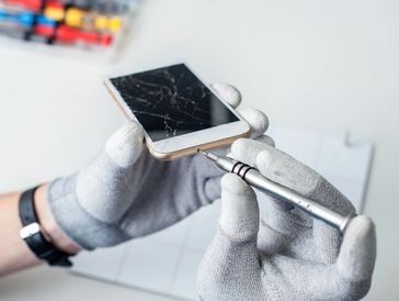 Technician in gloves examining a smartphone with a precision screwdriver.