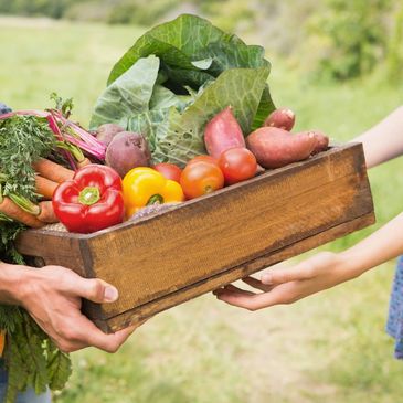 Two people exchanging a wooden crate full of fresh vegetables.