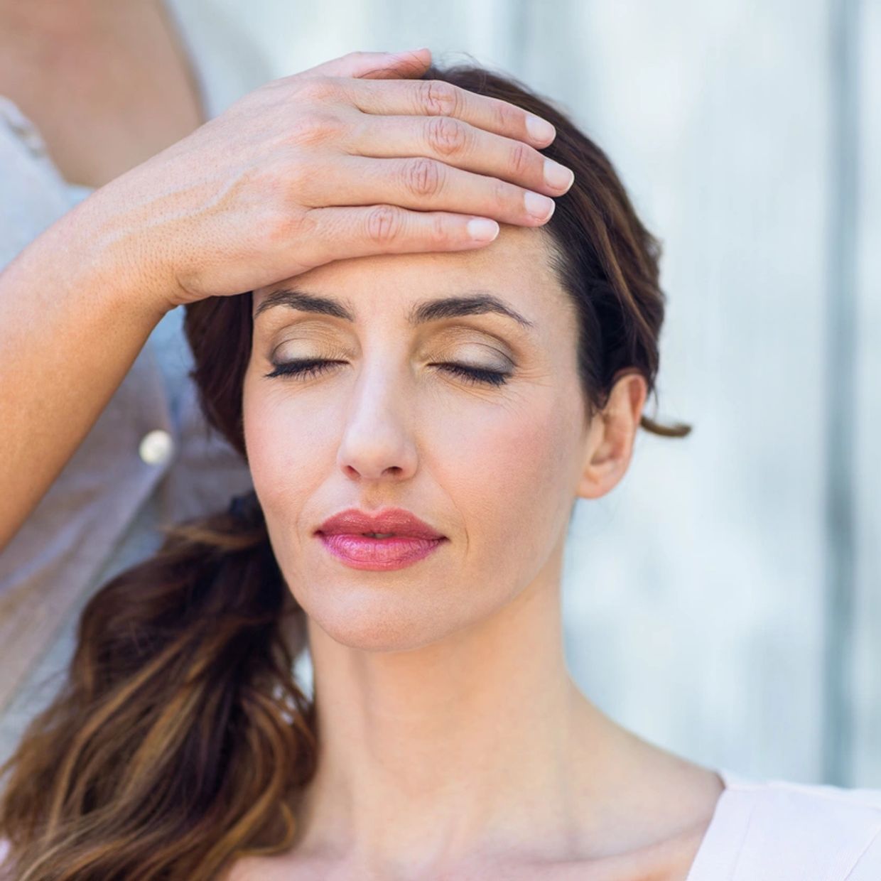 A woman enjoying tradition head massage with her eyes closed as a hand rests on her forehead. 