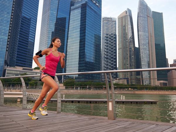 Woman running on a boardwalk with city skyscrapers in the background.