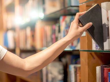 Person reaching for a book on a wooden shelf in a library.