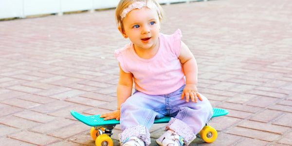 A toddler sitting on a bright blue skateboard with yellow wheels