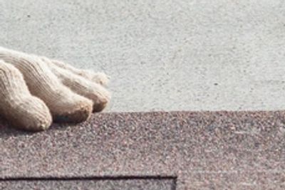 Hand in glove placing a shingle on a roof.