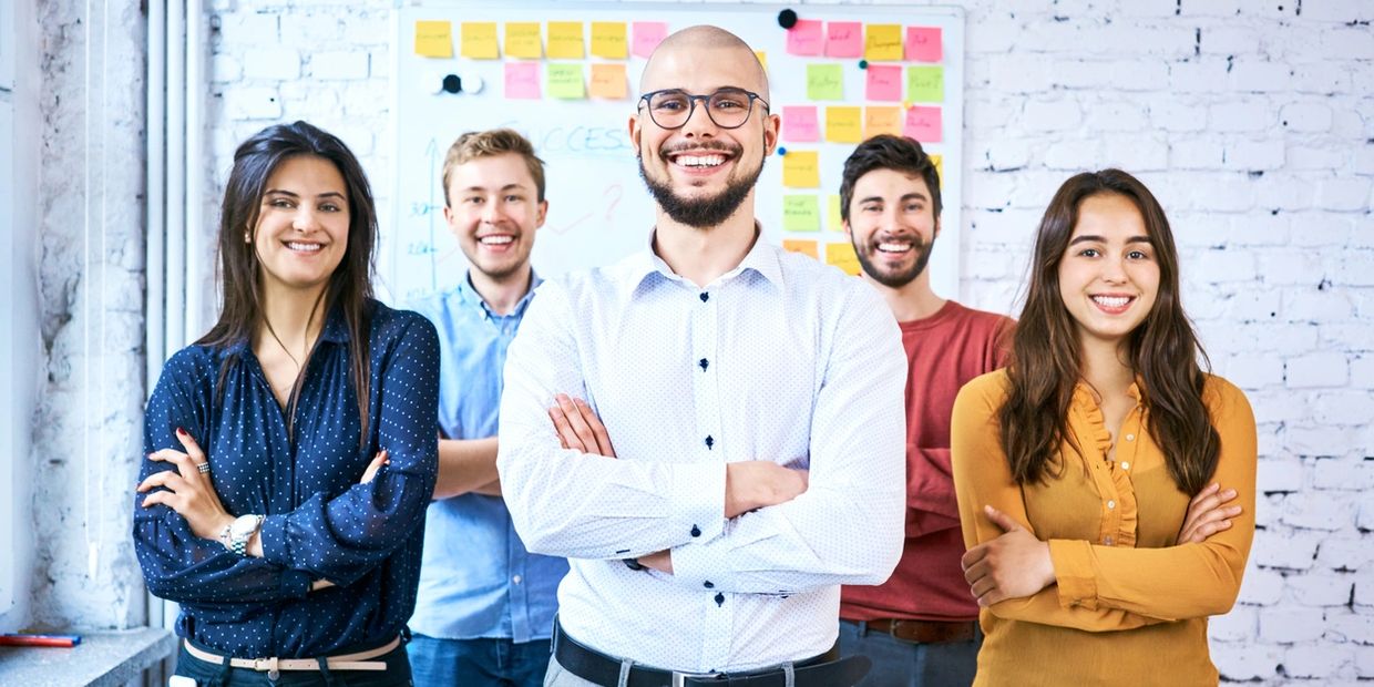 3 men and 2 woman standing in front of a work board smiling in pose for a photo