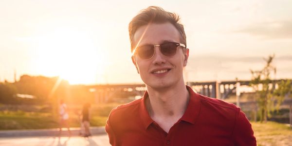 Young man wearing sunglasses and a red shirt at sunset.