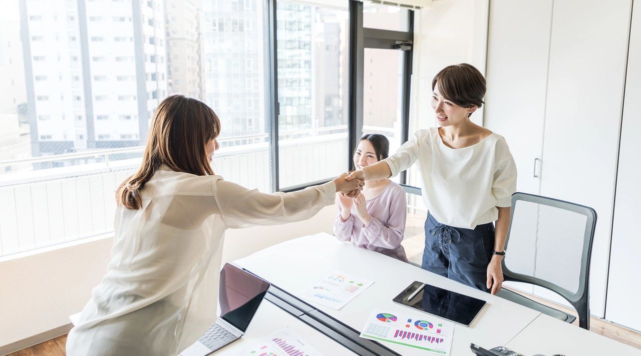 Two ladies smile and shake hands to close the deal in the office.