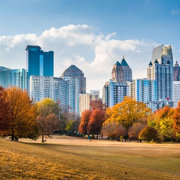 View of the skyline of Atlanta. In the foreground is a park and trees in autumn.