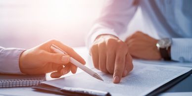 close up view of the hands of two individuals seated and reviewing a document.  One hold a pen.