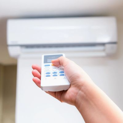 Hand holding remote control pointed at wall-mounted air conditioner.