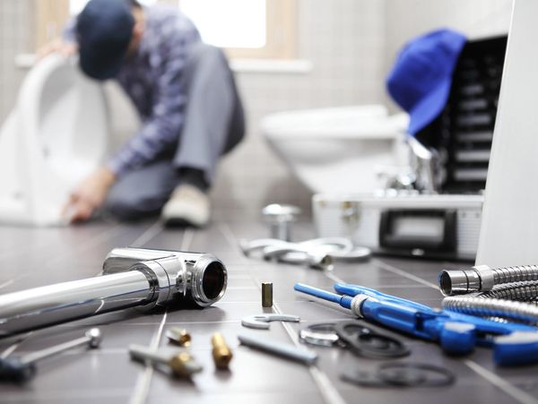 Plumber fixing a toilet with scattered tools in the foreground.