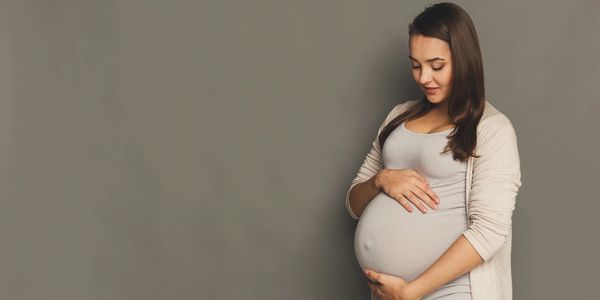 Pregnant woman gently holding her belly, smiling softly.