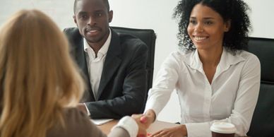 Stock photo of three people sitting at a table shaking hands in a meeting setting 