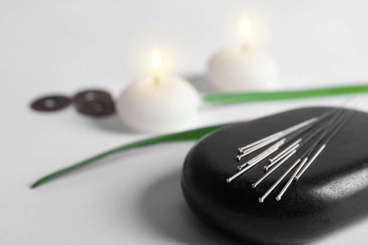 Acupuncture needles on a black stone with two white candles in the background. 