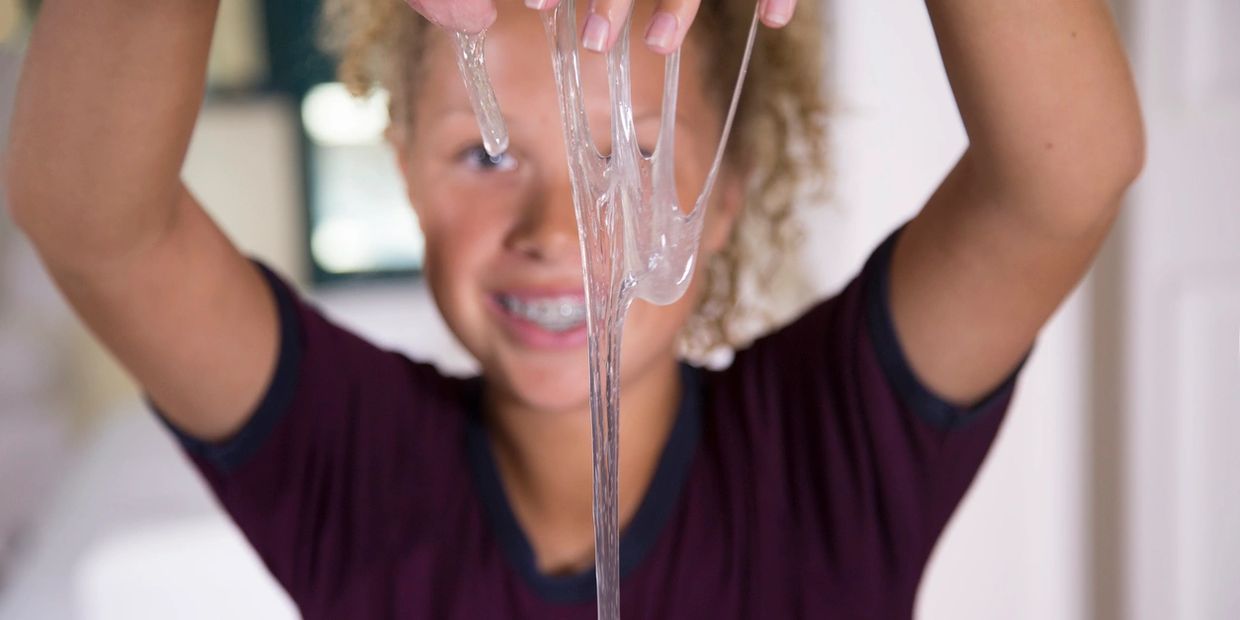 Child playing with clear slime, stretching it between fingers.