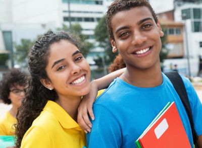 Two smiling students outdoors with books and backpacks.