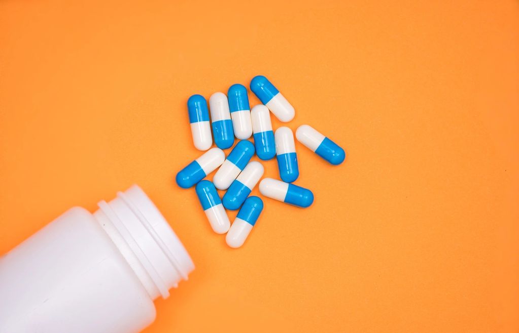 Blue and white capsules spilled from a white bottle on an orange surface.