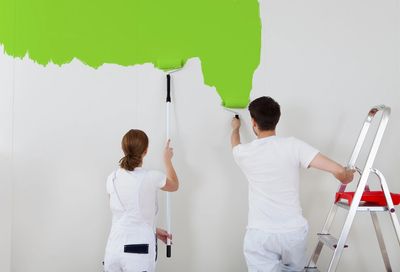 två personer målar grön färg på vit vägg