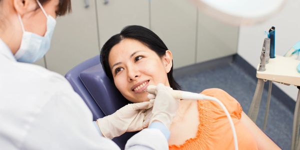 Image of a woman sitting on dental chair and dentist with electric brush in her hand