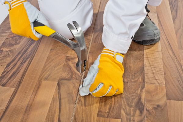 Person using a hammer and nail on wooden floor with gloves.