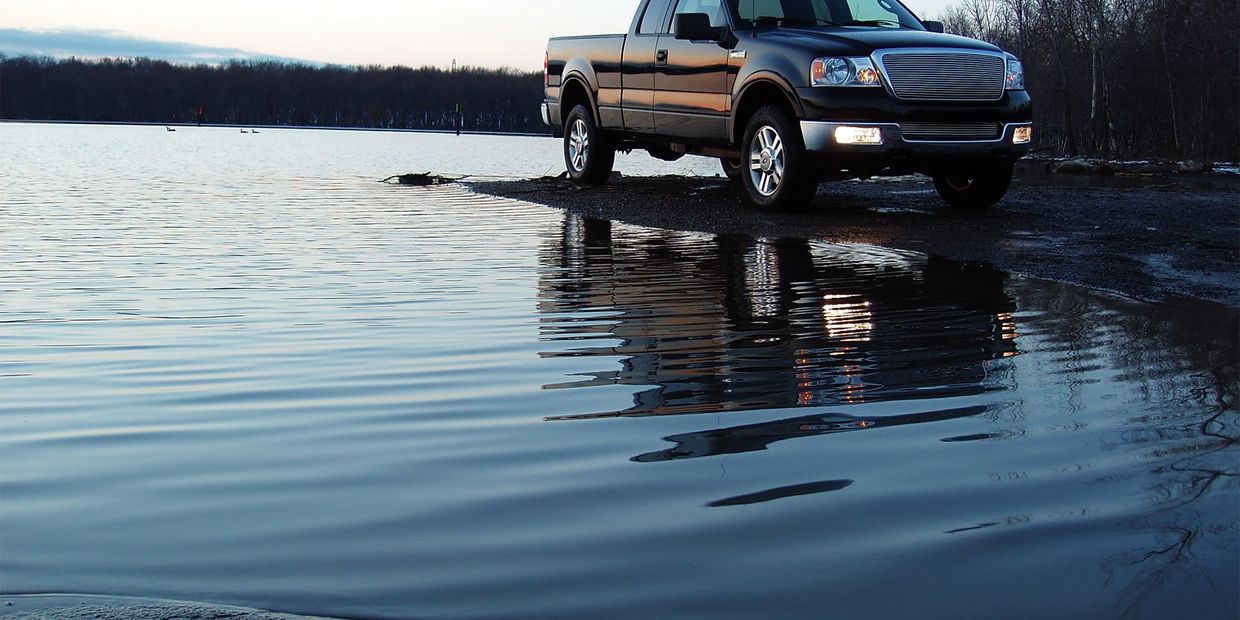 Black pickup truck parked by a calm lake at dusk.