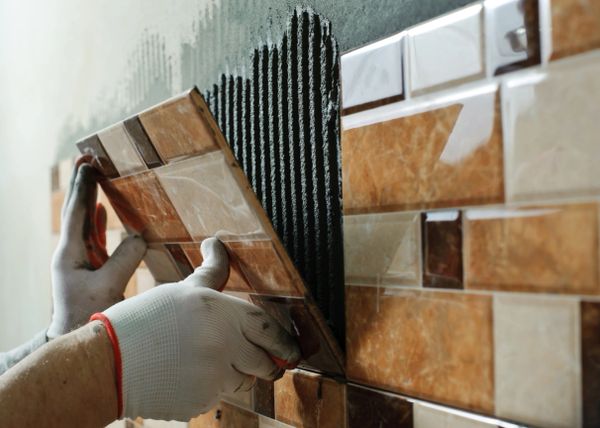 Hands installing brown ceramic wall tiles with adhesive.