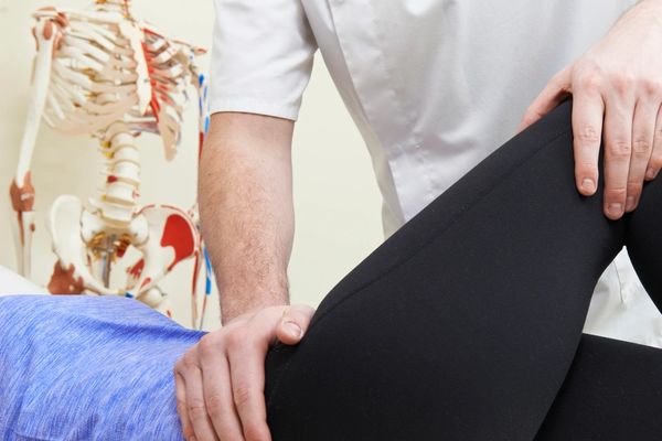 Physical therapist adjusting patient's bent leg during therapy session.
