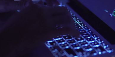 Hands typing on a glowing laptop keyboard in the dark.
