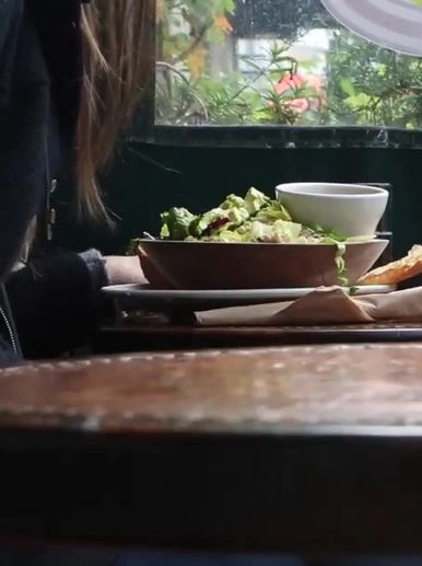 A person dining near a window with a fresh salad and bread on the table.
