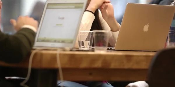 People working on laptops around a wooden table.